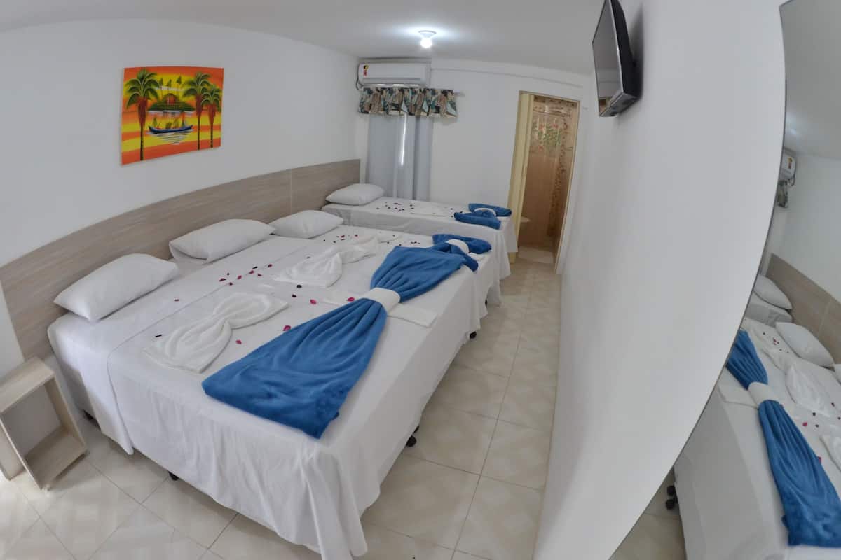 A hotel room with multiple beds, a TV mounted on the wall, and a painting of a sunset scene.