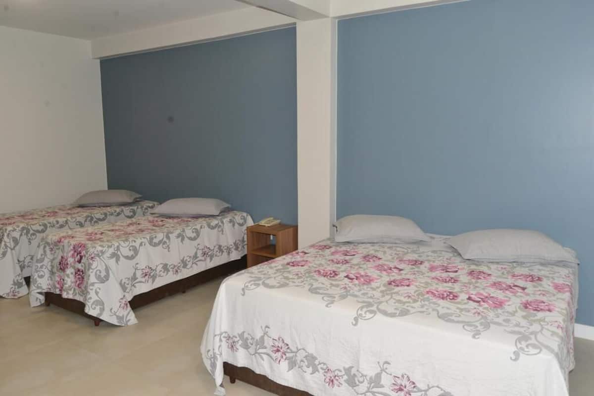 A room with two single beds, each with a floral bedspread and pillows. There is a small wooden nightstand with a lamp between the beds.