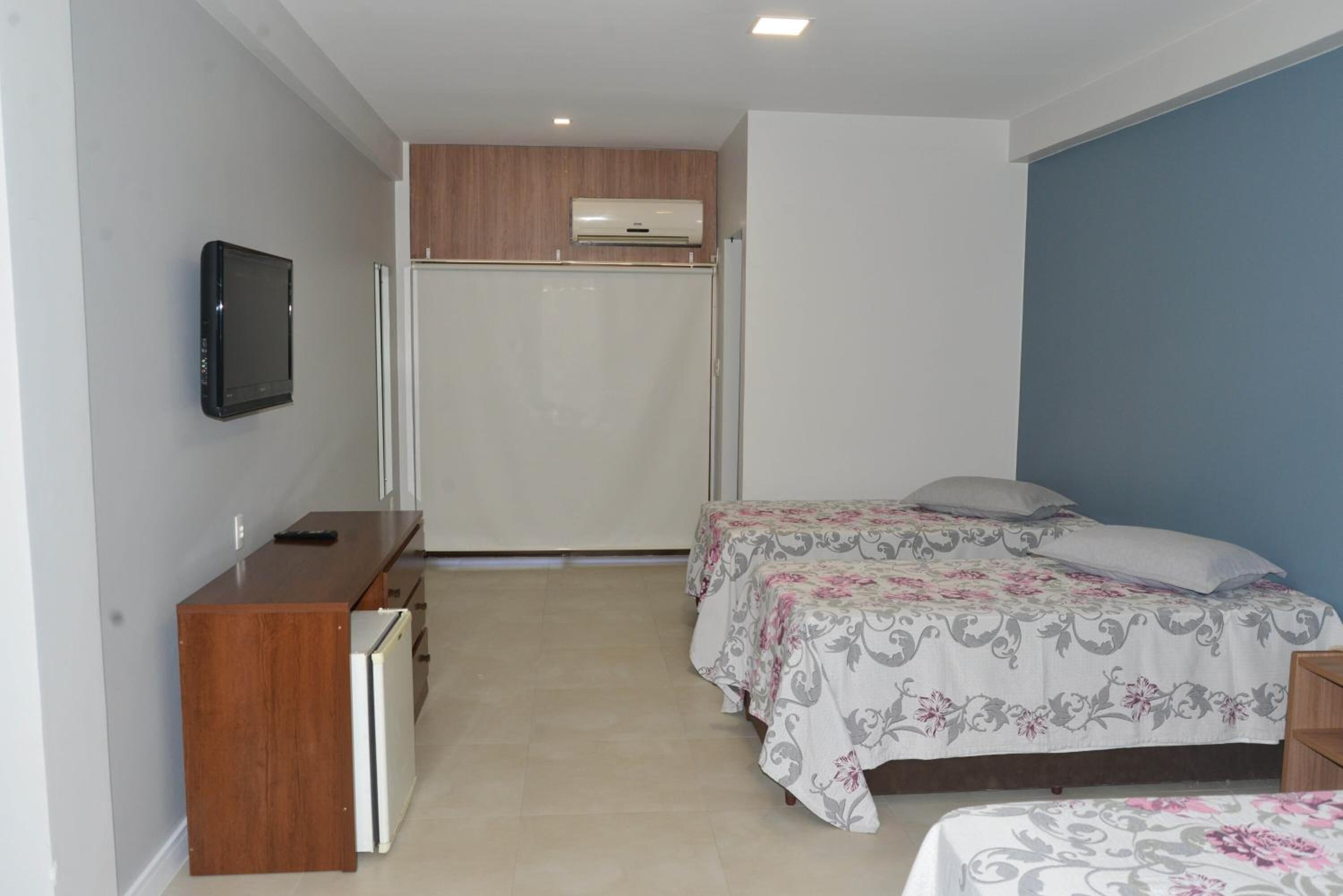A bedroom with two beds, a desk, a television, and an air conditioning unit.