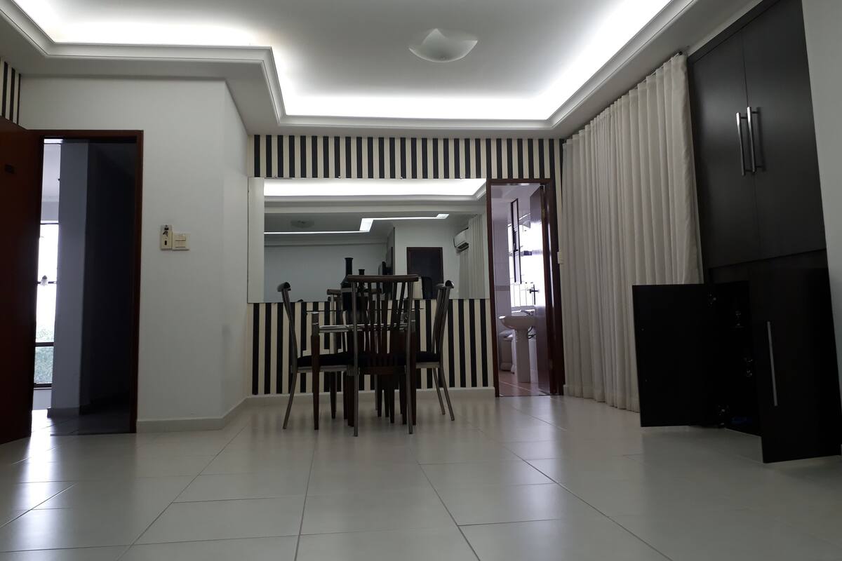 A modern kitchen with dark cabinets, a dining area with striped chairs, and a ceiling with recessed lighting.
