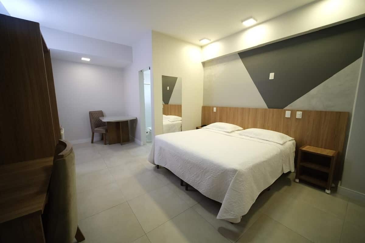 A modern hotel room with a bed, bedside tables, a desk, and a chair.