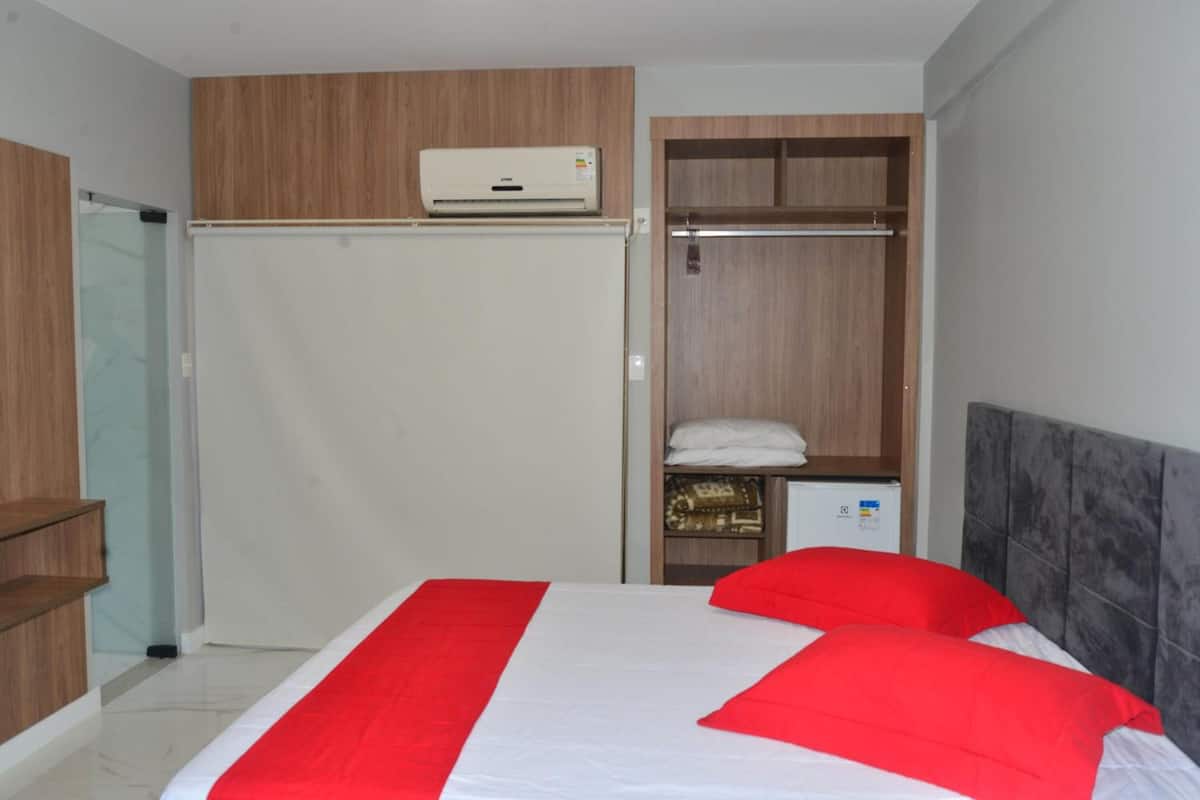 A bedroom with a bed, a wardrobe, a small heater, and a mirror.