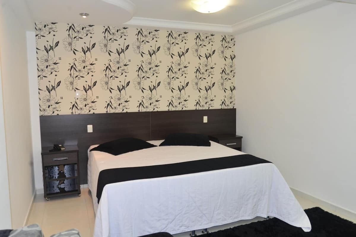 A bedroom with a bed, a nightstand, a dresser, and a floral wallpaper.