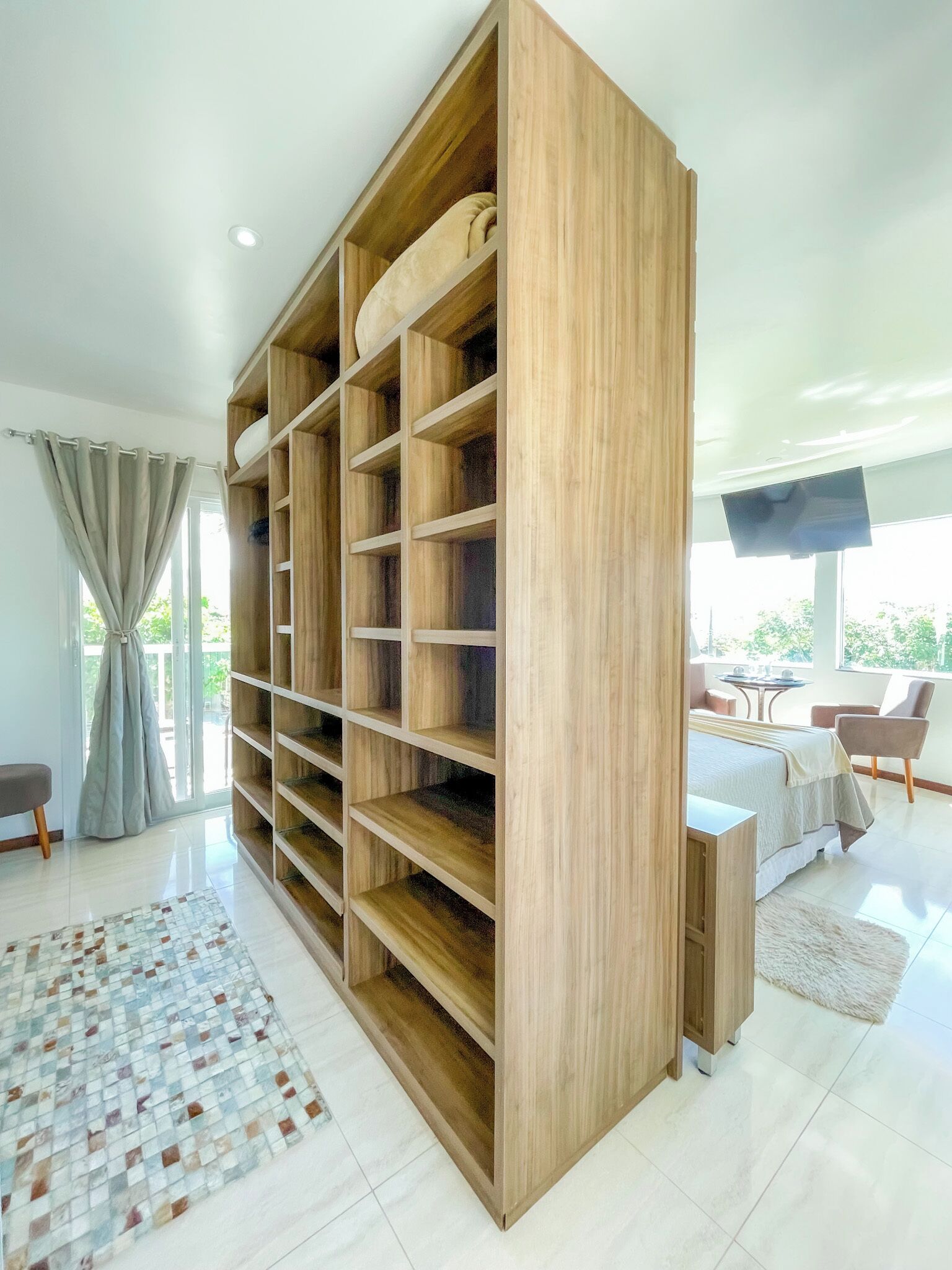 Una habitación moderna con una amplia estantería de madera, un comedor con mesa y sillas, y vistas al exterior con vegetación.