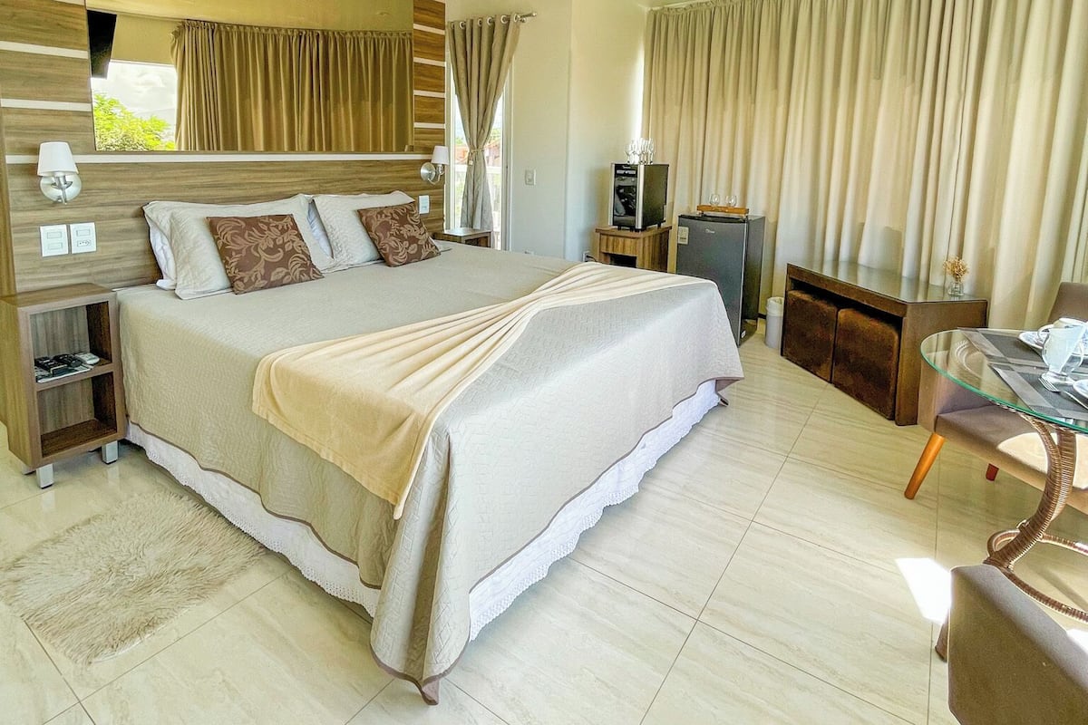 A modern bedroom with a large bed, a TV, a glass table, and a wooden nightstand.
