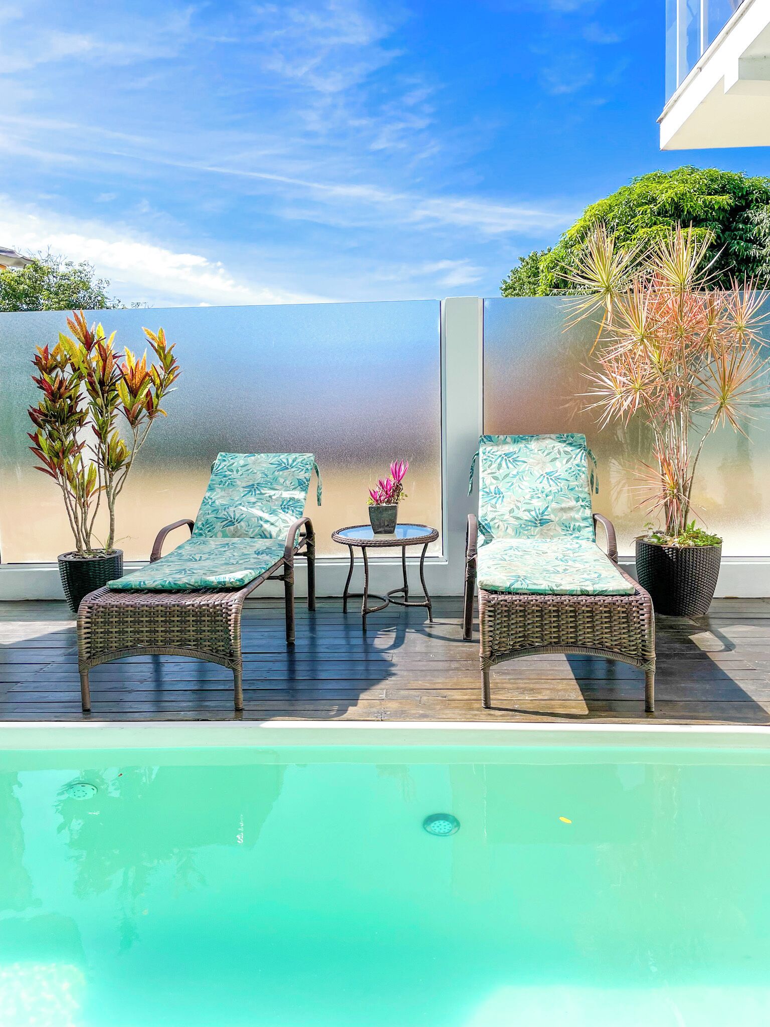 A poolside area with two wicker lounge chairs, a small table, and potted plants.