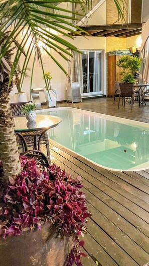 Un espace piscine doté d’une terrasse en bois, de chaises longues et de plantes en pot.