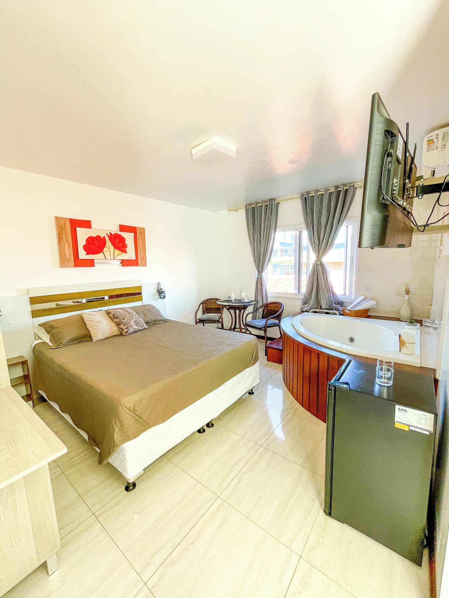 A hotel room with a bed, a small table, a chair, a sink, and a refrigerator.