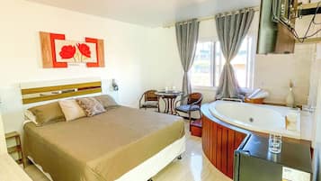 A hotel room with a bed, a small table, a chair, a sink, and a refrigerator.