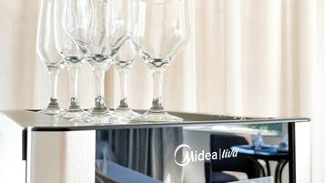 A minibar with three wine glasses on top, a minibar door with a logo, and a reflection of a room with a bed and curtains.