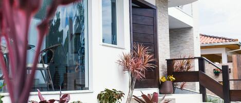 Una casa moderna con un ventanal grande, una escalera y varias plantas en macetas.