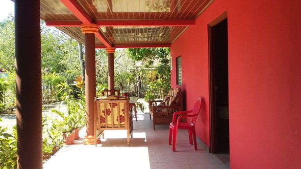 A covered patio with a red wall, wooden furniture, and potted plants. - Hospedaje Yaquelin (Cambutal)