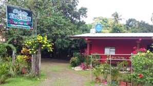 A red building with a signboard, surrounded by lush greenery and potted plants. - Hospedaje Yaquelin (Cambutal)