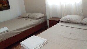 A room with two single beds, each with a pillow and a blanket. There is a small wooden nightstand between the beds. - Hospedaje Yaquelin (Cambutal)