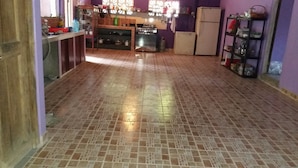 A kitchen with tiled flooring, a stove, a refrigerator, and shelves with various kitchen items. - Hospedaje Yaquelin (Cambutal)