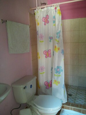 A bathroom with a toilet, a shower curtain with a butterfly and flower pattern, and a tiled floor. - Hospedaje Yaquelin (Cambutal)