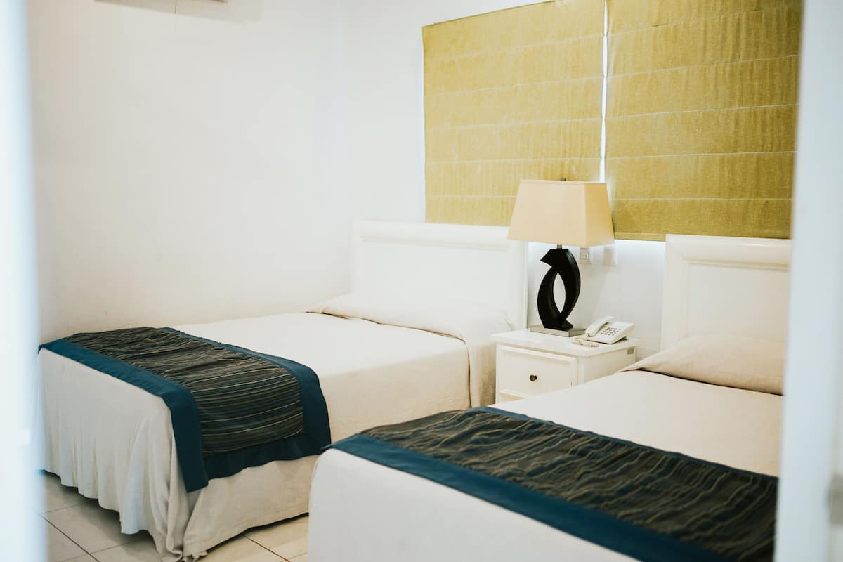 Una habitación de hotel con dos camas, una mesita de noche con lámpara y un teléfono.