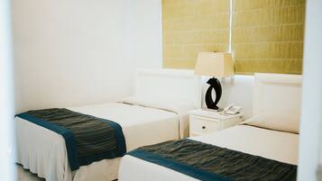 A hotel room with two beds, a nightstand with a lamp, and a telephone.
