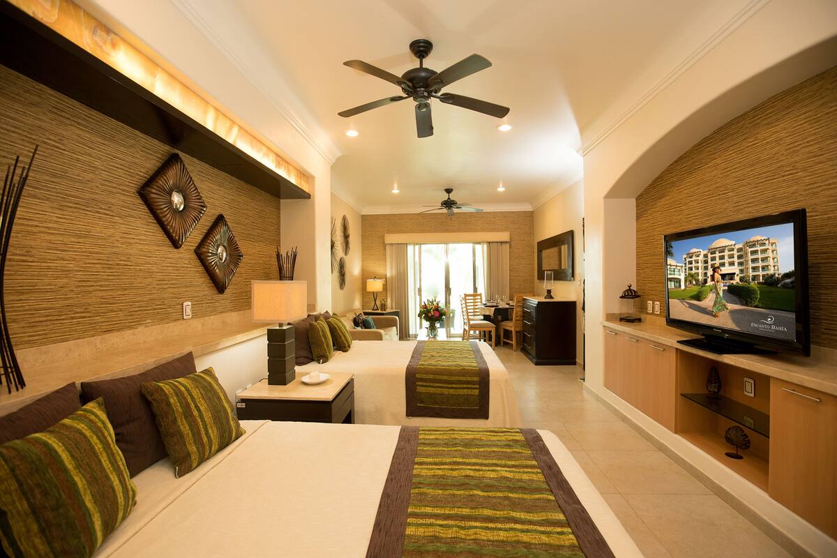 Habitación de hotel con una cama grande, televisión, ventilador de techo y vista al exterior del hotel.