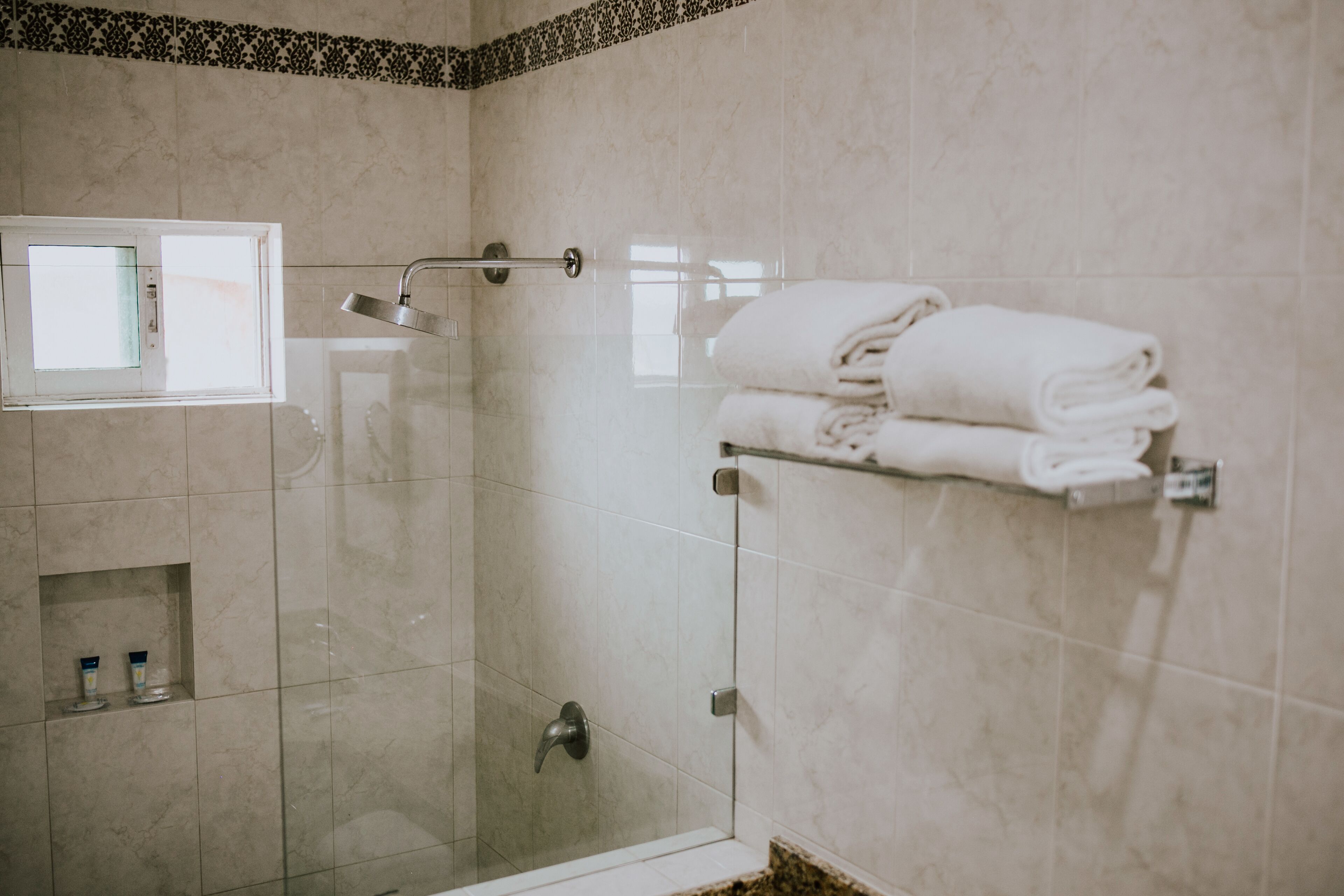 A modern bathroom with a glass shower enclosure, a towel rack with folded towels, and a small shelf with toiletries.