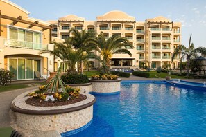 Un hotel con piscina, palmeras y un jardín cuidado.