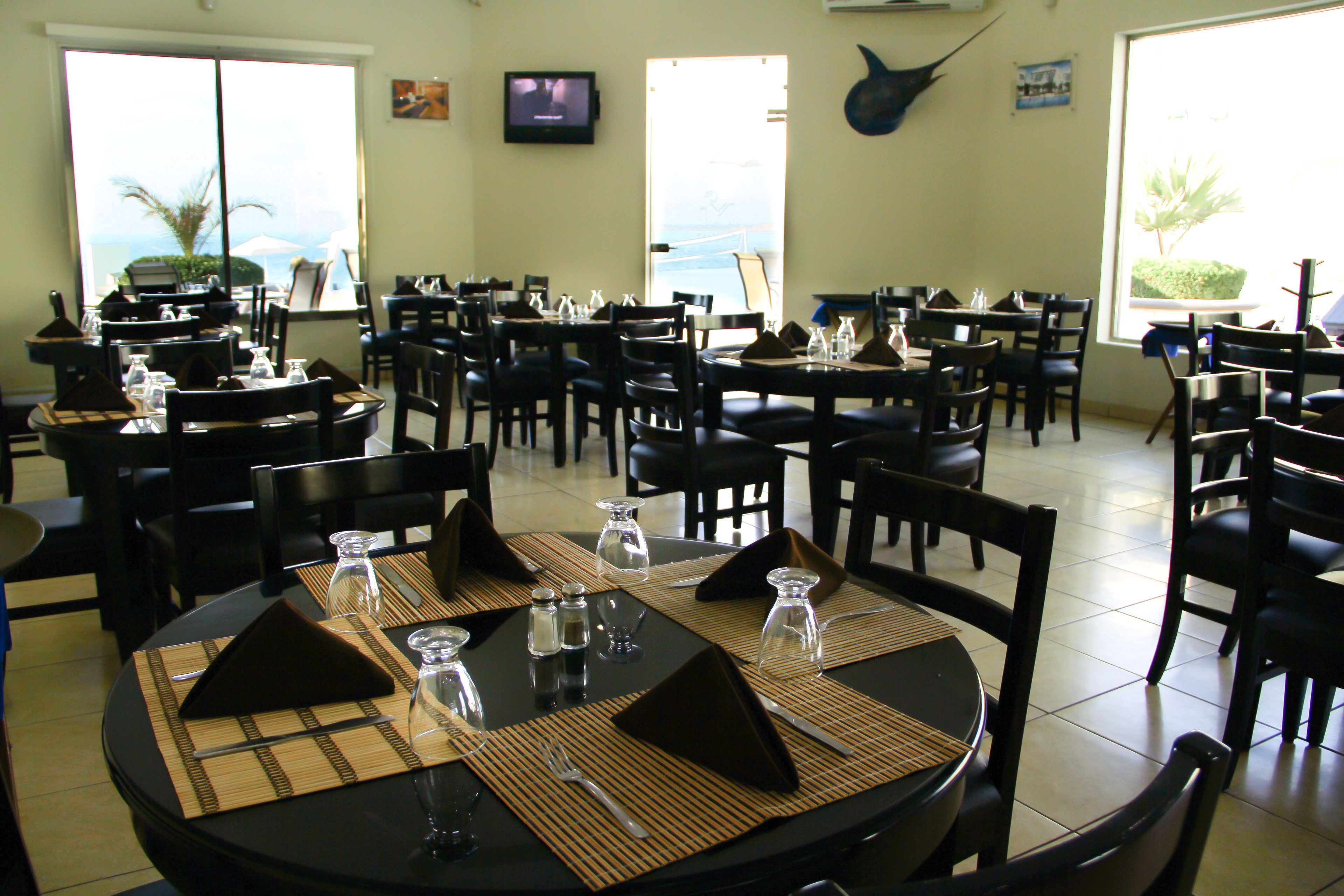 Un restaurante con varias mesas y sillas, dispuesto en un espacio amplio y con vista al océano a través de grandes ventanales.