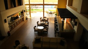 A spacious lobby with a high ceiling, a central seating area with sofas and round tables, and a staircase on the right. - Diamond Bay (Mazatlán)