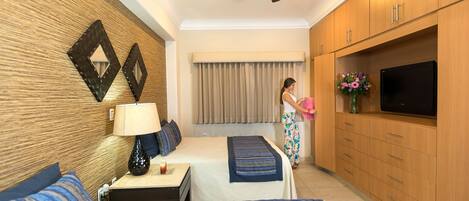 A hotel room with two beds, a ceiling fan, wooden cabinets, a TV, and a window with curtains.