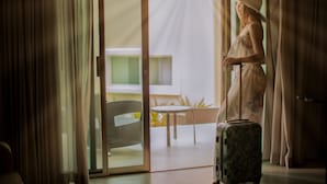 A room with a sliding glass door leading to a balcony, a wicker chair, and a suitcase. - Diamond Bay (Mazatlán)