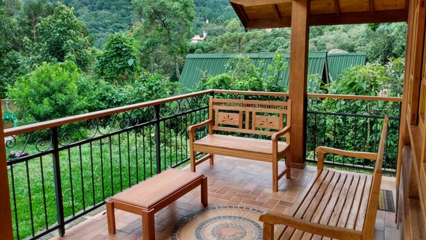 A wooden balcony with a bench and a table, overlooking a lush green landscape with trees and a mountain in the background. - Encanto Chalet-1.5 km from the center, 3 bedrooms, sleeps 8. Spectacular mountain view! (Monte Verde)