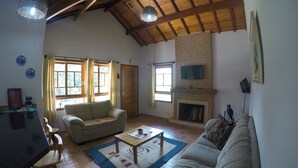A spacious living room with a high ceiling, a fireplace, a sofa, a coffee table, and a television mounted on the wall. - Encanto Chalet-1.5 km from the center, 3 bedrooms, sleeps 8. Spectacular mountain view! (Monte Verde)