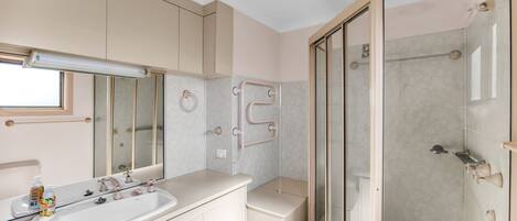 A modern bathroom with a large mirror, a sink with a soap dispenser, a shower with a glass door, and a towel rack.
