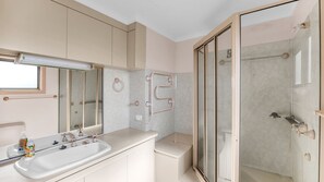 Une salle de bain moderne avec un grand miroir, un lavabo doté d’un distributeur de savon, une douche avec une porte en verre et un porte-serviettes.