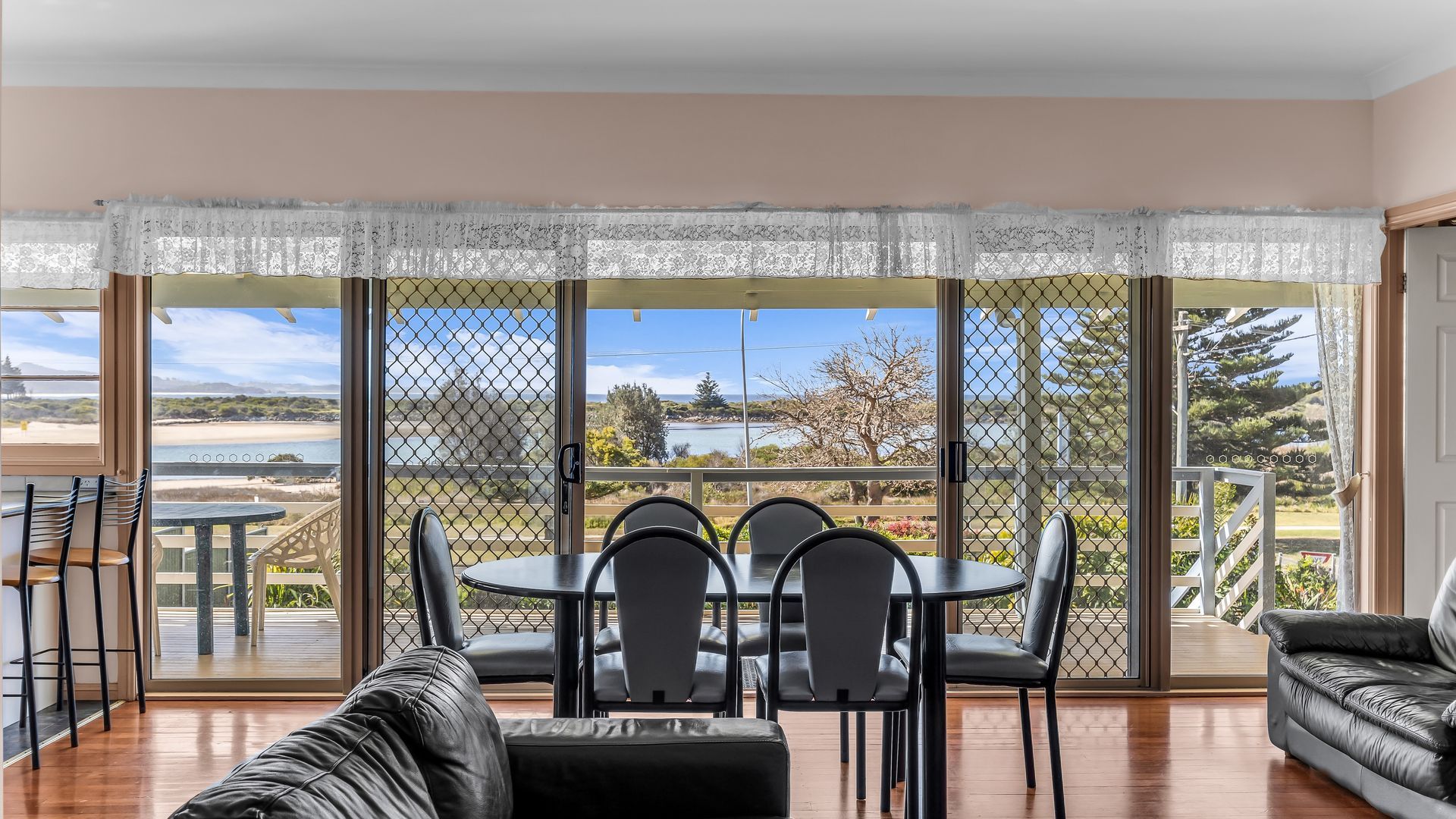 A dining area with a table and chairs, a sofa, and a view of the beach through large windows.