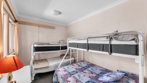 Une chambre avec un lit superposé, un lit simple et un bureau avec une lampe.