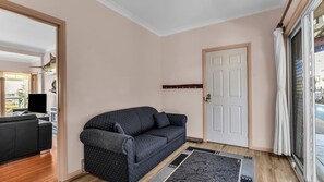 Un salon avec un canapé à motifs sombres, un plancher en bois, une porte blanche et une vue sur l’extérieur à travers une porte vitrée.