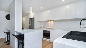 Una cocina moderna con armarios blancos, un refrigerador de acero inoxidable, horno integrado y un lavamanos negro.