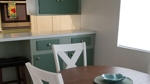 Ein Essbereich mit Holztisch, weißen Stühlen, einem grünen Schrank und einem Fenster mit Tageslicht.