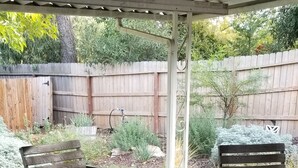 Eine Terrasse im Freien mit einem Holztisch und -stühlen, umgeben von einem Holzzaun und Grünpflanzen.