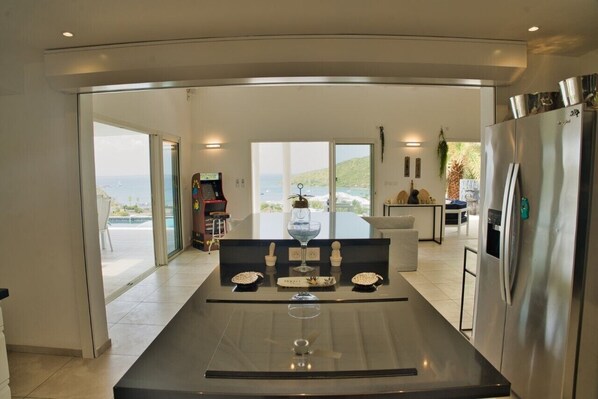 A modern kitchen with a central island, large windows, and a view of the sea.