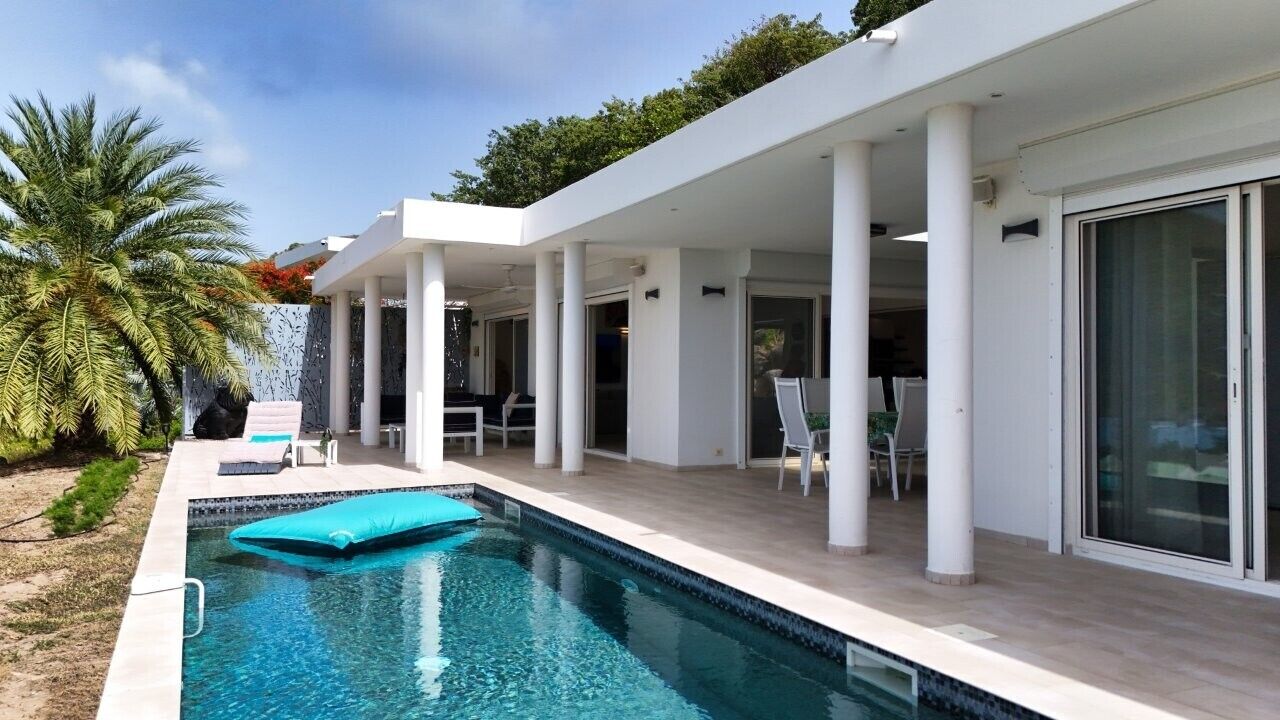 A modern house with a swimming pool, outdoor seating, and a covered patio area.
