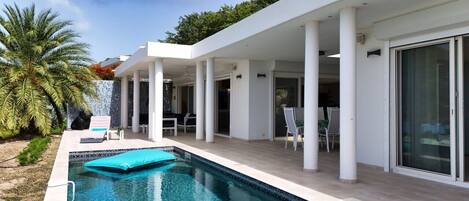 A modern house with a swimming pool, outdoor seating, and a covered patio area.