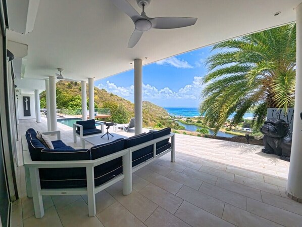 A covered outdoor seating area with a pool view, white columns, and a statue.