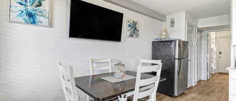 A dining area with a table, chairs, a TV, and a refrigerator.