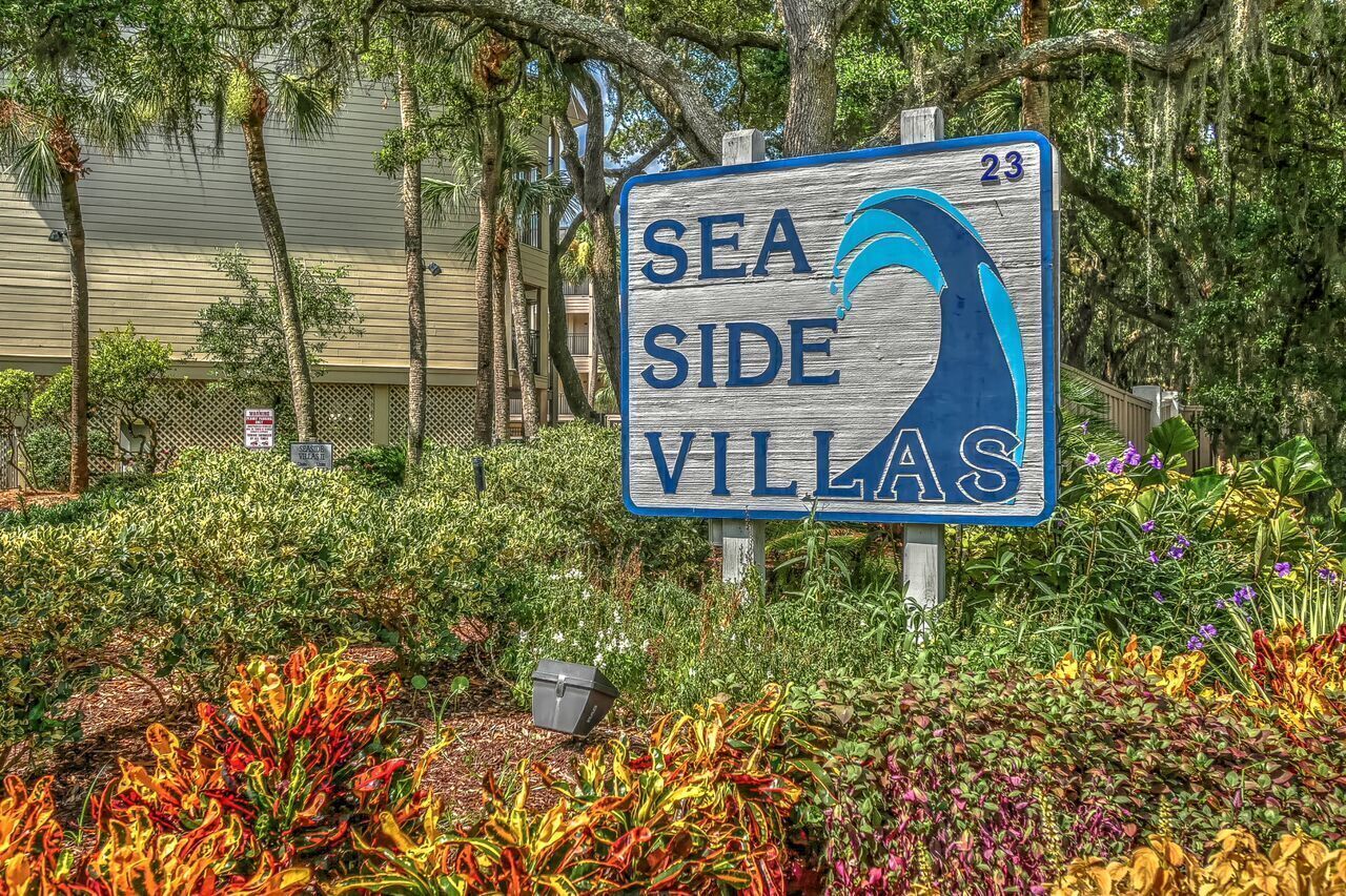 A sign for 'Sea Side Villas' with a wave symbol, surrounded by lush greenery and palm trees.