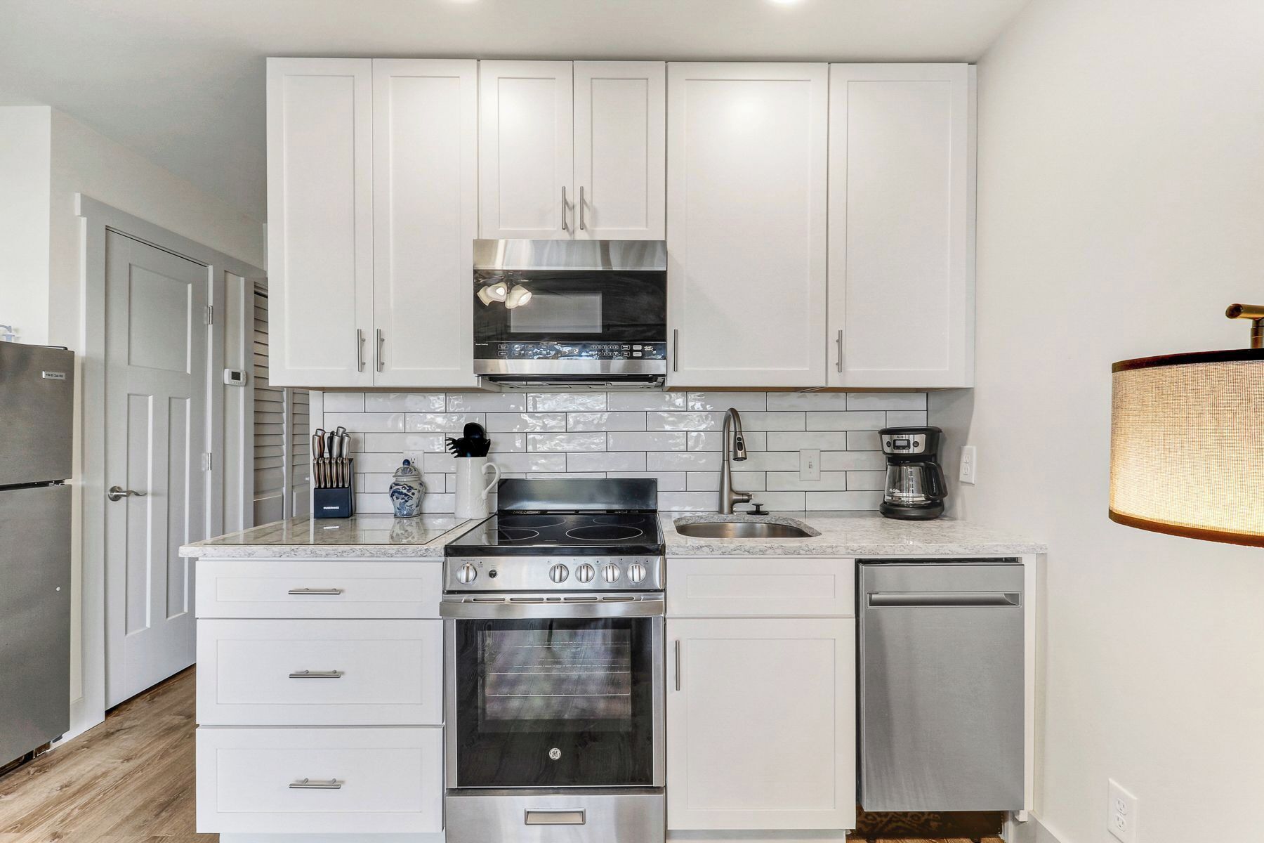 A modern kitchen with white cabinets, a stainless steel range, an oven, a dishwasher, and a microwave.