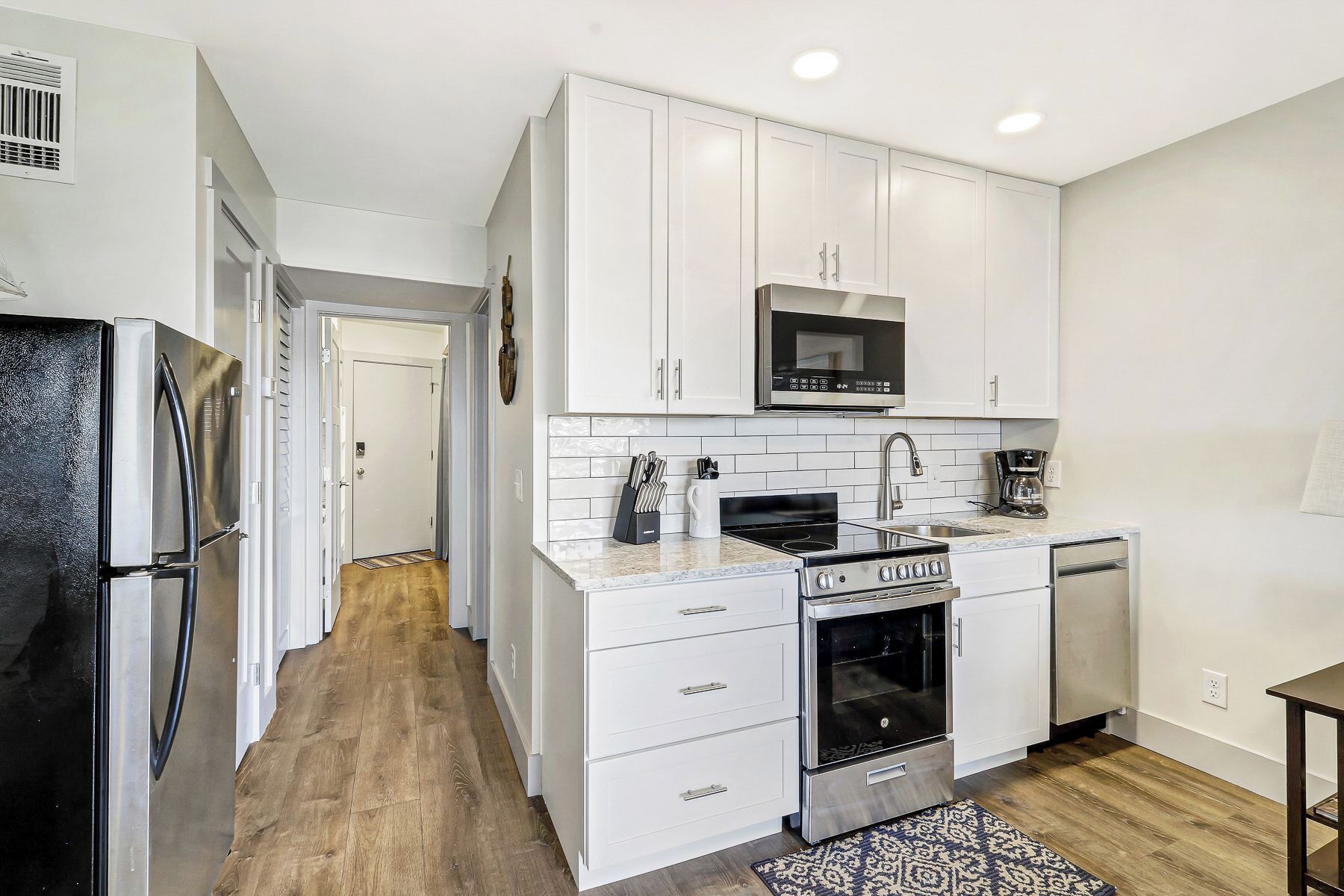 A modern kitchen with white cabinets, a stainless steel refrigerator, a microwave, an oven, and a coffee maker.