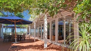 En udendørs terrasse med overdækket siddeområde, et bord med stole og en stor parasol.