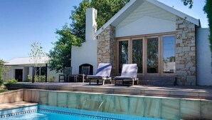 Et moderne hus med swimmingpool, stenvæg og to liggestole.