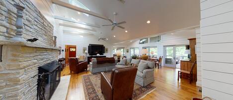 A spacious living room with a stone fireplace, a ceiling fan, and a large TV.